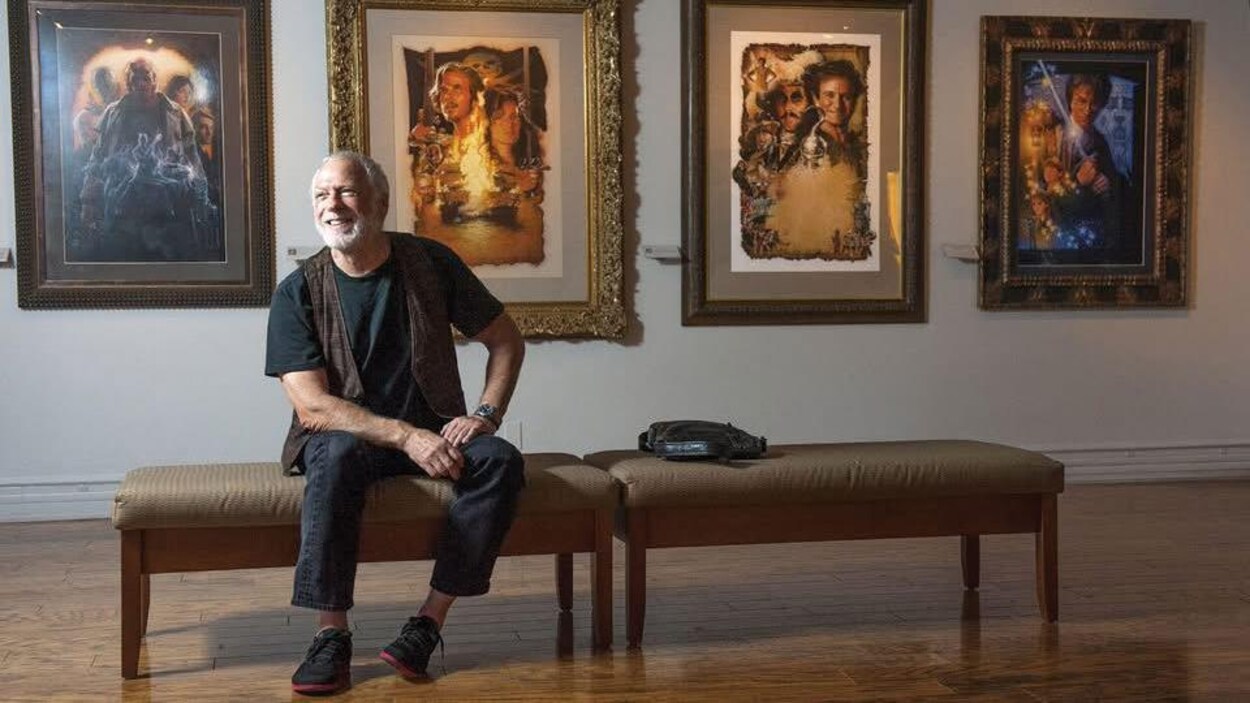 Drew Struzan posant devant plusieurs de ses affiches.